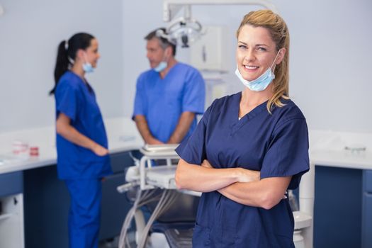 Smiling nurse with arms crossed and co-workers behind her
