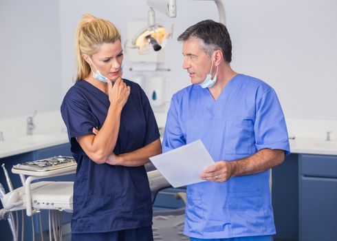 Thoughtful co-workers talking about a file attentively in dental clinic