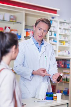 Pharmacist pointing a flask of pills in front of a customer in the pharmacy