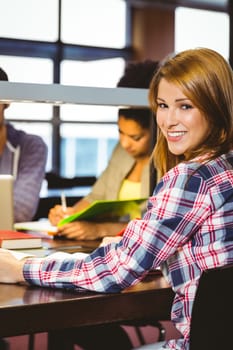 Portrait of a smiling student sitting at desk looking at camera in library