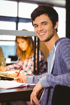 Portrait of a smiling student sitting at desk looking at camera in library