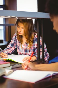 Serious student sitting at desk writing in notepad in library