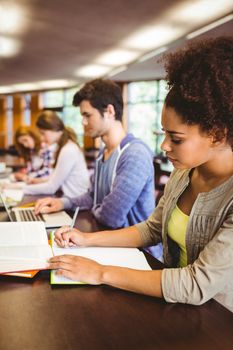 Focused students sitting in a line writing in library