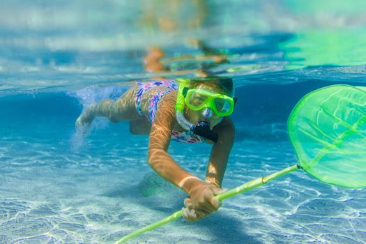 Underwater shoot of a cute girl snorkeling with scoop-net in a tropical sea