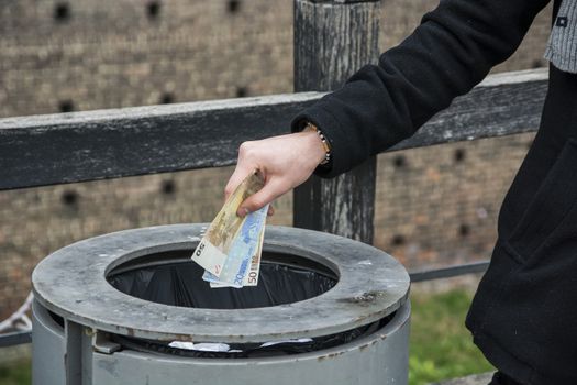 Hand of young man outdoors throwing euro banknotes in a can, conceptual image