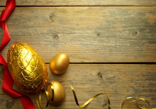 Golden easter eggs with decoration ribbon over a wooden backdrop