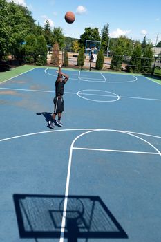 Basketball player shooting the ball at the basket on an outdoor court.