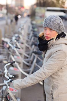 Lady dialing on keyboard of urban bicycle station. Bikes for rent. Green sustainable ecological public transport. Healthy lifestyle.