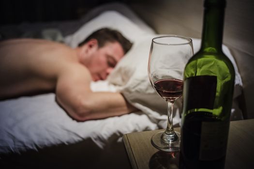 Hangover Man in a Bed at Night with a Wine Bottle in foreground