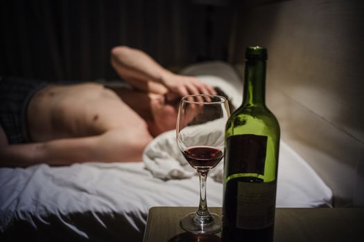 Hangover Man with Headaches in a Bed at Night and Wine bottle in Focus