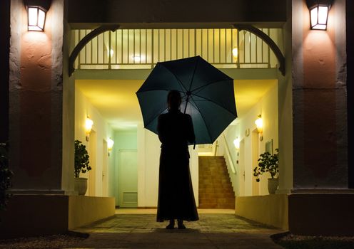 Woman in Silhouette Holding Umbrella In Front of Apartment Entrance
