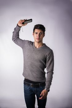 Attractive young man throwing away remote control with disgusted expression, standing on white