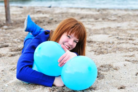 redheaded girl with balloons laying on the sand