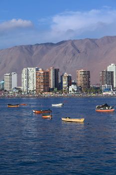 IQUIQUE, CHILE - JANUARY 23, 2015: View from the peninsula at the end of Cavancha beach over the fishing boats anchoring in the bay, Cavancha beach and the modern tall buildings along Arturo Prat Chacon Avenue on January 23, 2015 in Iquique, Chile. Iquique is a popular beach town and free port city in Northern Chile. 