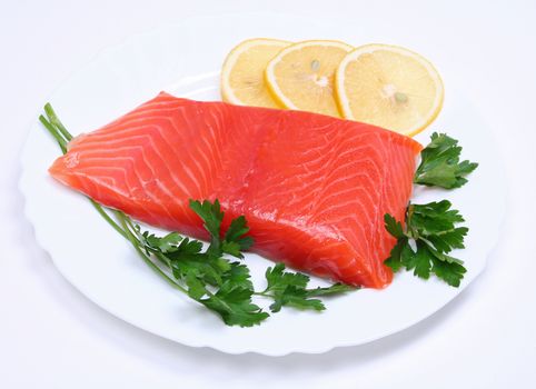 Salmon steak with lemon slices and parsley on white plate