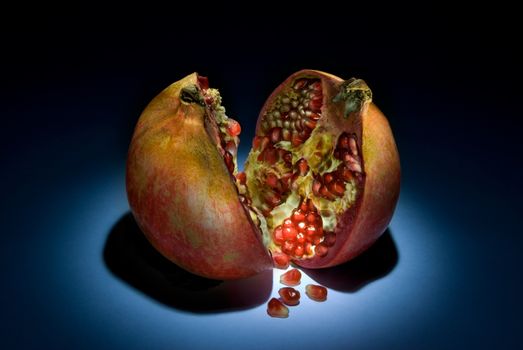 Two parts of a pomegranate on a dark background. Beautiful art illumination.