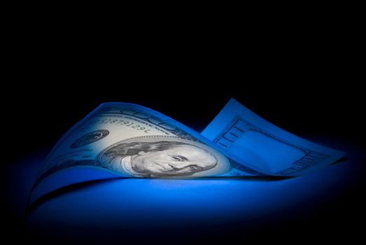 Hundred dollars. Dark blue art illumination.
Black background. 