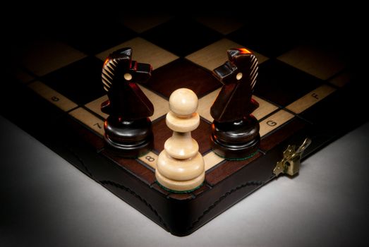 Chessmen on a chess board. A dark background and art illumination.