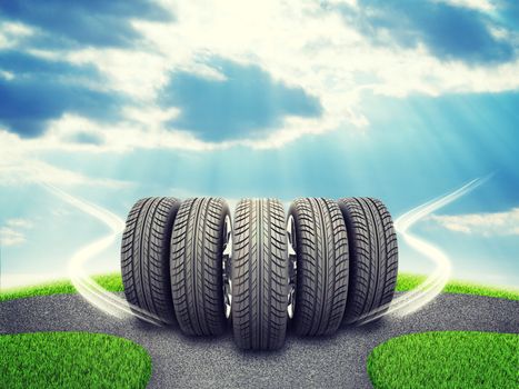 Wedge of new car wheels. Road fork  and green grass field. Sky with clouds and sun beams in background