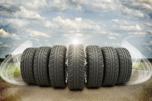 Wedge of new car wheels on old road. Roadsides, green grass field and abstract smoke. Sky with clouds in background