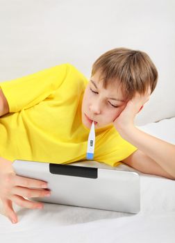 Sick Kid with Tablet Computer and Thermometer on the Bed