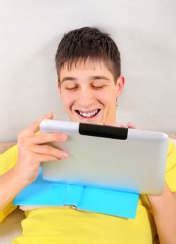 Cheerful Student with a Book and Tablet Computer on the Bed