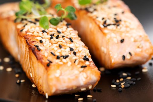 Grilled salmon, sesame seeds  and marjoram on a black plate. Studio shot