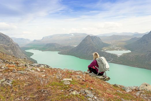 Hiker with backpack relaxing on cliff of a mountain and enjoying valley and lake view at Jotunheimen National Park, Norway