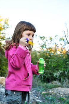 little girl blowing soap bubbles in autumn forest 