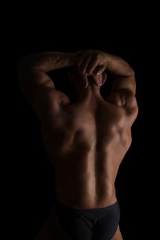 Handsome shirtless bodybuilder showing huge back isolated on black background. Sports and fitness.