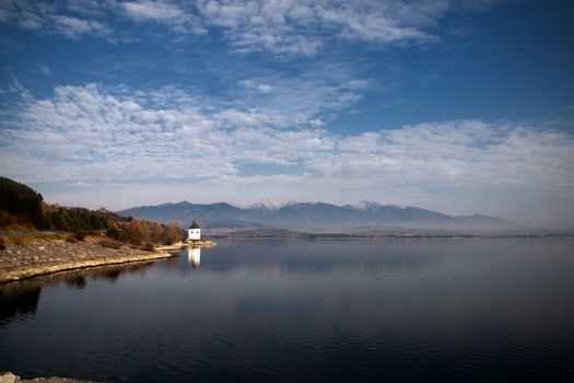 Chapel on the shore of a lake with mountains on the background