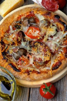 Homemade Pizza with Edible Mushrooms, Tomatoes, Salami and Grated Cheese on Circle Cutting Board and Ingredients on Wooden background. Top View