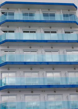 Modern Apartment Building with Blue Glass Facade, Balcony and Windows with Reflection of Skies closeup Outdoors