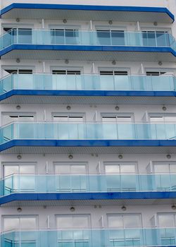 Modern Apartment Building with Blue Glass Facade, Balcony and Windows with Reflection of Skies closeup Outdoors