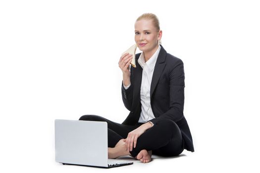 blonde businesswoman seated on the floor with computer and eating a sandwich