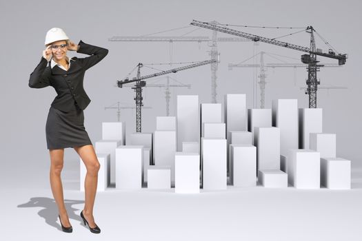 Business woman in suit, helment and glasses, smiling. Full lenght. Many white cubes with wire-frame tower cranes on gray background