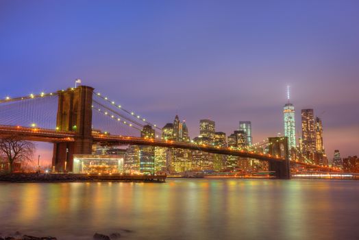 Brooklyn bridge and New York City Manhattan downtown skyline at dusk with skyscrapers illuminated over East River panorama. Copy space.