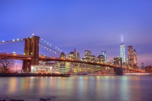 Brooklyn bridge and New York City Manhattan downtown skyline at dusk with skyscrapers illuminated over East River panorama. Copy space.