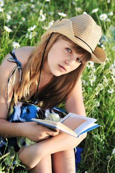 reading girl wearing hat sitting on the meadow