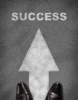 Top view of shoes standing on asphalt road with arrow and word success. Business concept
