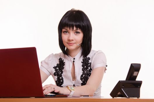 Pretty girl sitting in a call center with a laptop in a white blouse with black embroidery