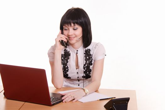 Cute little girl sitting at a table in a call center with a laptop in a white blouse with a phone in his hand