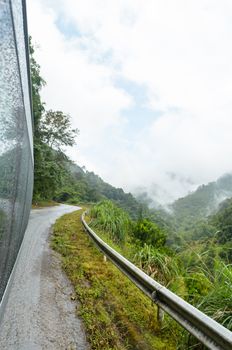Travel with a van on road in the forest and mountain amidst morning fog of Thailand