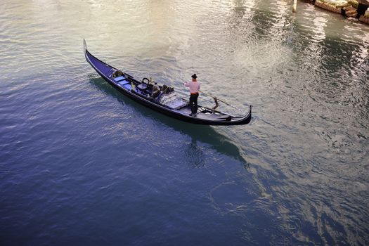 A typical gondolier wearing the white and red striped shirt brings two tourists along the canals of Venice, Italy