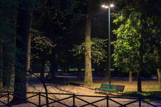 A solitary bench of a park illuminated during evening time