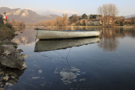 An old boat reflected on the rived with the mountains in the background. Brivio d’Adda, Milan, Italy