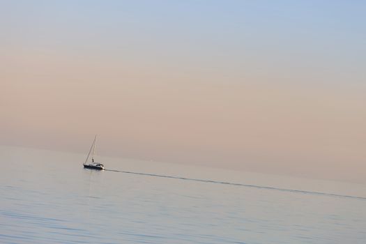 A calm and suggestive scenario with a sailboat navigating at sunset