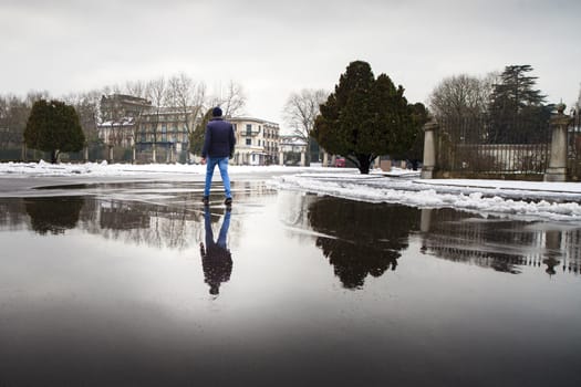 A young man and his reflection walking on a pluddle during a winter cold day