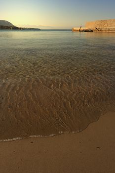 A piece of sandy bay illuminated by the sun with a boat in the background, Cefalu, Italy 