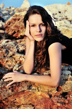 brunette girl laying on the cliff at sunset time